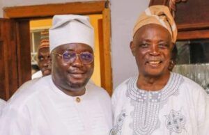 The Stool Is Bigger Than The Ballot: Why Traditional Rulers Must Stay Non-Partisan Two men in traditional West African attire posing and smiling for a photo indoors, one wearing a white agbada and cap with glasses, the other in a patterned tunic and tan cap.