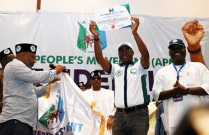 Gov. Makinde Emerges APM Consensus Presidential Candidate Man in white shirt and cap raises a certificate on a stage as others applaud, a banner reading 'People's Movement' behind them indicating an awards ceremony or recognition event.