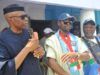 Tinubu’s Performance Influenced My Defection To APC—Mimiko Three men at a public event: the leftmost man in a black cap and dark clothing speaks into a microphone, while two others in colorful outfits and caps stand beside him.