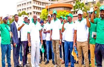 NOA, CIPMN Advocate Mandatory Licensing For Project Management Practice Through Awareness Walk Group of people in green and white shirts standing together outdoors, some raising fists in the air. Crowded in front of a building.