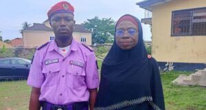 NGO Partners Oyo NOA On Civic Re-Engineering, Responsible Citizenship Man in a purple security uniform with a red beret stands next to a woman wearing a black hijab outdoors near buildings and grass.