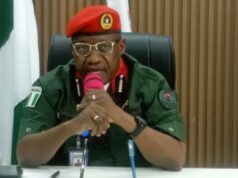Oyo NSCDC Agro Rangers Neutralise 1 Suspected Criminal; Arrest Two Others In Iseyin Military officer in a green uniform and red beret speaking into a pink microphone at a desk in a conference room, with flags in the background.