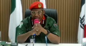 Oyo NSCDC Agro Rangers Neutralise 1 Suspected Criminal; Arrest Two Others In Iseyin Military officer in a green uniform and red beret speaking into a pink microphone at a desk in a conference room, with flags in the background.