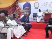 OYRLEA Holds Farmers, Herders Dialogue On Enforcement On Open Grazing Officials seated on a red-carpeted stage at a government event, with a moderator speaking into a microphone on a podium in the background.