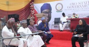 OYRLEA Holds Farmers, Herders Dialogue On Enforcement On Open Grazing Officials seated on a red-carpeted stage at a government event, with a moderator speaking into a microphone on a podium in the background.