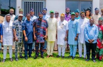 Ogundoyin Leads Oyo Lawmakers To Endorse Bimbo Adekanmbi As APM Governorship Aspirant Group of diverse adults standing on a lawn in front of a building, wearing colorful traditional attire and smiling.
