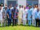 Ogundoyin Leads Oyo Lawmakers To Endorse Bimbo Adekanmbi As APM Governorship Aspirant Group of diverse adults standing on a lawn in front of a building, wearing colorful traditional attire and smiling.