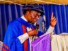 Ojo-Lanre Charges IIJ Matriculating Students to Embrace Development Journalism in the Age of Phone Journalism Man in blue academic gown and cap delivering a speech at a podium, microphone in hand, raising one finger.