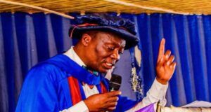 Ojo-Lanre Charges IIJ Matriculating Students to Embrace Development Journalism in the Age of Phone Journalism Man in blue academic gown and cap delivering a speech at a podium, microphone in hand, raising one finger.