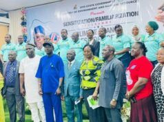 Oyo Trains Climate Change Desk Officers Across The State Group of diverse officials and attendees posing for a formal group photo indoors, with a banner and a line of people in teal uniforms visible in the background.