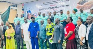 Oyo Trains Climate Change Desk Officers Across The State Group of diverse officials and attendees posing for a formal group photo indoors, with a banner and a line of people in teal uniforms visible in the background.