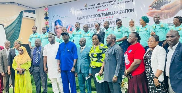Oyo Climate Group of diverse officials and attendees posing for a formal group photo indoors, with a banner and a line of people in teal uniforms visible in the background.