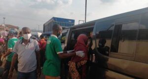 Makinde’s Govt, Security Agencies Clear Ibadan Streets of Destitutes, Beggars A man in a green shirt helps a woman in a red headscarf board a dark bus/van as others wear masks nearby in a busy transport scene.
