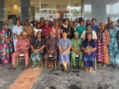 Oyo PHC Board Advances Family Planning Through SHINE Project Large diverse group of adults in colorful traditional clothing posing for a group photo outside a glass-front building; some seated in front and others standing behind them.