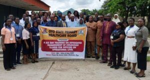 Makinde’s Govt Trains Health Officers On Childhood Illness Management Group of healthcare workers and officials posing outdoors with a banner for an Oyo State health board training event on childhood illness management.