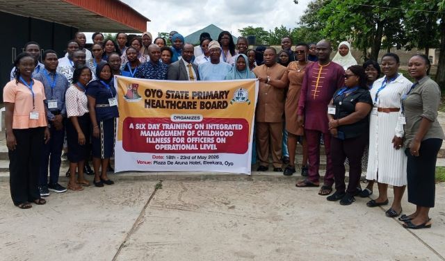 Oyo Primary Health Group of healthcare workers and officials posing outdoors with a banner for an Oyo State health board training event on childhood illness management.