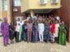Oyo PHC Board Begins Adaptation of National Safe Pregnancy Termination Guidelines Large diverse group of men and women posing for a group photo outside a brick building with a yellow overhang and air conditioning units above.