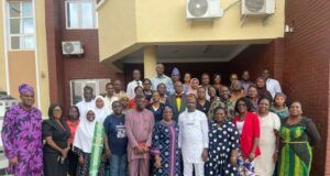 Oyo PHC Board Begins Adaptation of National Safe Pregnancy Termination Guidelines Large diverse group of men and women posing for a group photo outside a brick building with a yellow overhang and air conditioning units above.