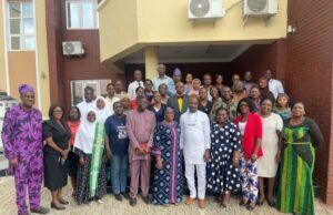 Oyo PHC Board Begins Adaptation of National Safe Pregnancy Termination Guidelines Large diverse group of men and women posing for a group photo outside a brick building with a yellow overhang and air conditioning units above.