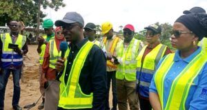 RAAMP: Oyo Govt Completes 88.02 Km Of Rural Roads, Markets In Phase One Of Project Group of people in high-visibility vests at a construction site, a man in a cap speaks into a microphone while others listen.
