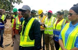 RAAMP: Oyo Govt Completes 88.02 Km Of Rural Roads, Markets In Phase One Of Project Group of people in high-visibility vests at a construction site, a man in a cap speaks into a microphone while others listen.