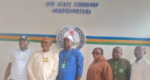 SYDI DG, POCACOV Southwest Chairman Visit Oyo CP Over Abduction In Oriire Six people stand side by side in front of a wall reading 'OYO STATE COMMAND HEADQUARTERS,' with a circular emblem and colored stripes behind them.