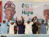 2027: Oyo APC Leaders Adopt Alli As Consensus Governorship Candidate Group of diverse speakers on a stage at a political rally, raising their hands in solidarity in front of a banner that reads 'Renewed Hope' and campaign imagery.