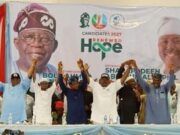 2027: Oyo APC Leaders Adopt Alli As Consensus Governorship Candidate Group of diverse speakers on a stage at a political rally, raising their hands in solidarity in front of a banner that reads 'Renewed Hope' and campaign imagery.