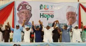 2027: Oyo APC Leaders Adopt Alli As Consensus Governorship Candidate Group of diverse speakers on a stage at a political rally, raising their hands in solidarity in front of a banner that reads 'Renewed Hope' and campaign imagery.