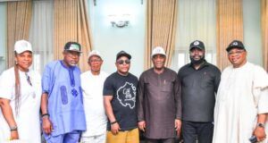 Oyo City Boy Movement Secures Support From Senator Yunus Akintunde Eight people standing together indoors in front of beige curtains, posing for a group photo in varied traditional and casual outfits.