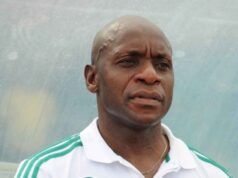 Reasons Abia Warriors Collapsed In 2025/2026 NPFL Top Three Race—Shorunmu Man with a shaved head wearing a white polo with green stripes, looking to the side outdoors against a blue background.