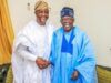 Tinubu Took Tough Decisions Past Leaders Avoided — Sunday Dare Two men wearing white and blue agbadas shake hands and smile in a living room setting.