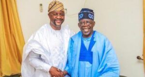 Tinubu Took Tough Decisions Past Leaders Avoided — Sunday Dare Two men wearing white and blue agbadas shake hands and smile in a living room setting.
