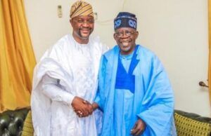 Tinubu Took Tough Decisions Past Leaders Avoided — Sunday Dare Two men wearing white and blue agbadas shake hands and smile in a living room setting.
