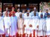 I’m Happy States No Governors Struggle To Pay Salaries—Tinubu Group of men in traditional Nigerian attire posing for a photo on a red carpet at an Eid celebration, with floral decorations in the background.