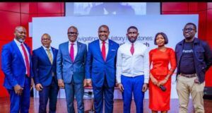 At Pan African Confab, UBA Reaffirms Interest In Deeper Bank-Fintech Collaboration Seven professionals posing on a stage for a conference photo, dressed in suits and a red dress.