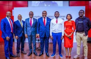 At Pan African Confab, UBA Reaffirms Interest In Deeper Bank-Fintech Collaboration Seven professionals posing on a stage for a conference photo, dressed in suits and a red dress.