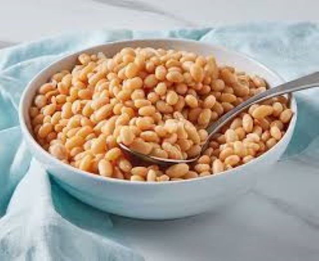 beans White bowl filled with cooked chickpeas and a metal spoon resting in them on a light blue cloth