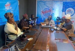 Men in traditional attire sit around a radio studio table speaking into microphones with Splash FM banners behind them