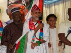 APC-South Africa Inaugurates Mpumalanga Executives, Strengthens Mobilisation For 2027 Election Man in white traditional robe speaks into a microphone at a cultural event, draped in a green, red, and white flag with others nearby.