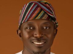 Oyo Warns Residents Of Flash Floods, Calls For Strict Adherence To Safety Measures Portrait of a smiling man wearing a colorful striped headwrap and white traditional attire against a warm brown background.