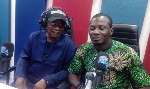 Akeem Abas 2 Two people sit at a radio studio desk with microphones and headphones, mid-conversation.