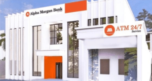 How We Posted ₦1.9 Billion PBT In First 10 Months Of Operations – Alpha Morgan Bank Exterior of an Alpha Morgan Bank branch with white modern facade, orange accents, and an ATM-24/7 service sign.