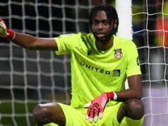 Leicester City Targets Super Eagles Goalkeeper Soccer goalkeeper in a neon yellow kit crouches in front of the goal, wearing red gloves and pointing with one arm at the left side.