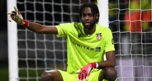 Leicester City Targets Super Eagles Goalkeeper Soccer goalkeeper in a neon yellow kit crouches in front of the goal, wearing red gloves and pointing with one arm at the left side.