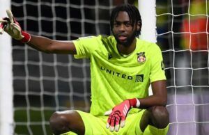Leicester City Targets Super Eagles Goalkeeper Soccer goalkeeper in a neon yellow kit crouches in front of the goal, wearing red gloves and pointing with one arm at the left side.