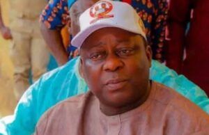 Osun Accord Chairman Shot, Police Begin Probe Man wearing a beige traditional outfit and a white cap sits with a blue water bottle nearby, looking to the side.