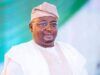 Barr Akeem Agbaje Condemns Abduction Of Adelabu’s Sister, Twin Sons Smiling man in white traditional attire and cap with glasses, posed against a green backdrop.
