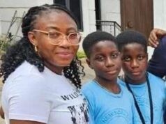 Alli Condemns Ex-Minister Adelabu’s Sister’s Abduction, Urges Swift Rescue Three people posing for a photo outside a building: an adult woman with glasses and two young boys in blue shirts, all smiling at the camera.