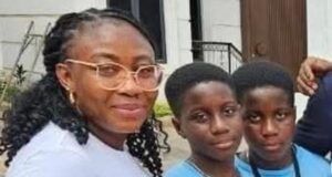 Alli Condemns Ex-Minister Adelabu’s Sister’s Abduction, Urges Swift Rescue Three people posing for a photo outside a building: an adult woman with glasses and two young boys in blue shirts, all smiling at the camera.